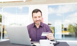 Mid adult man using online banking service to transfer money between accounts using laptop in shopping mall