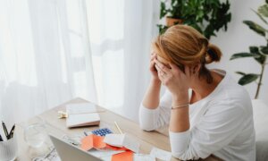A women looking over at a desk with a laptop and has her hands clasped.