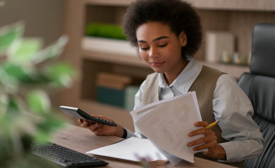 Woman sitting at a desk, reading, with papers in her hand.