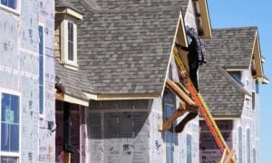 A worker on a ladder works on the exterior of a new home under construction.