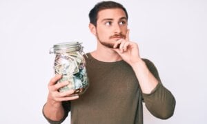 A young man stands holdings a jar full of money