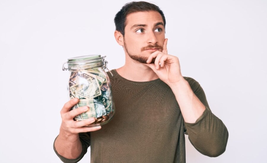 A young man stands holdings a jar full of money