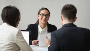 Smiling female CEO wearing glasses talking with company subordinates, discussing business strategies. Colleagues negotiating in positive atmosphere, working at laptops. Cooperation, leadership concept