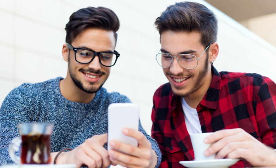 Two young people at a cafe smile at a smartphone.