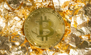 A gold bitcoin sits on top of crinkled gold paper