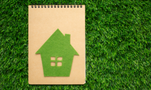 A house cut from green felt sits on a notebook on grass