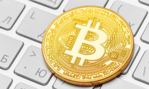 A gold bitcoin sits on a computer keyboard
