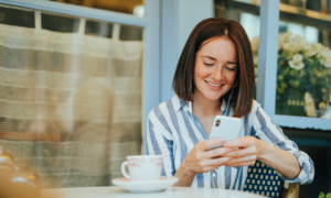 A smiling young woman checks her account balance on her phone