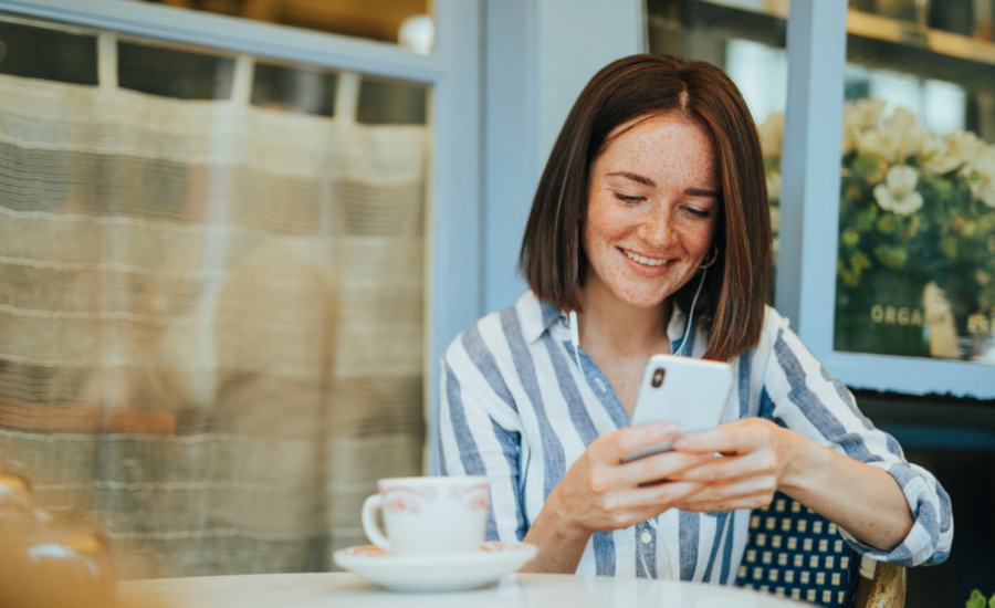 A smiling young woman checks her account balance on her phone