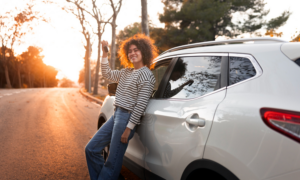 A smiling woman leans against an SUV parked on a road
