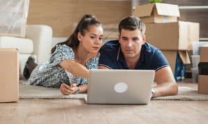A man and woman use a laptop in their half-packed living room