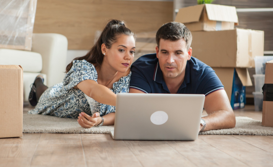 A man and woman use a laptop in their half-packed living room