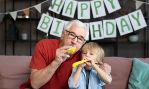 A grandfather and grandson sit in front of a Happy Birthday sign.