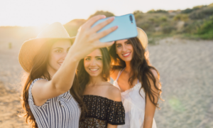 Three young women take a selfie on a beach.