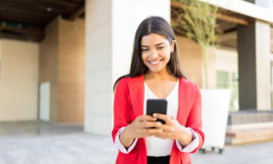 Young woman smiles at her phone outside a building