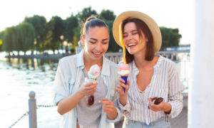Two young women eat ice cream coins on a waterfront