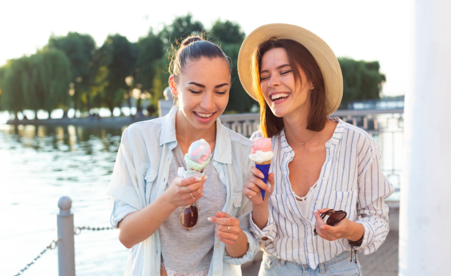 Two young women eat ice cream coins on a waterfront