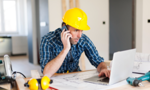 A contractor in a hard hat checking his computer and talking on his phone