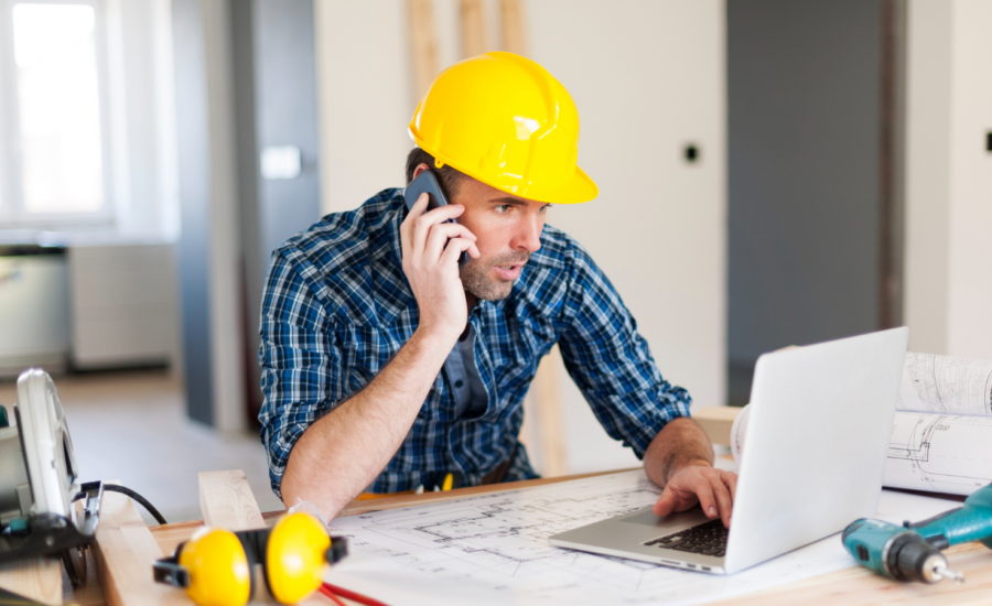 A contractor in a hard hat checking his computer and talking on his phone