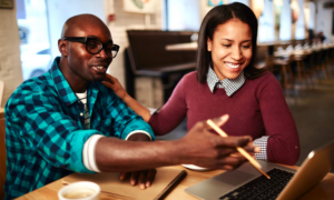 A young man and woman look at a laptop in a cafe